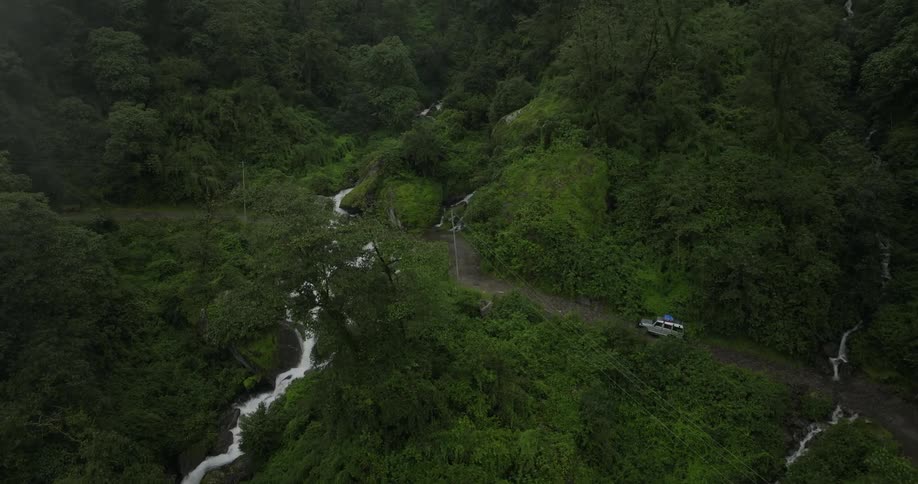 White jeep drives on road through mountain forest near waterfall
