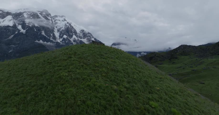 A grassy hill surrounded by snowcapped mountains
