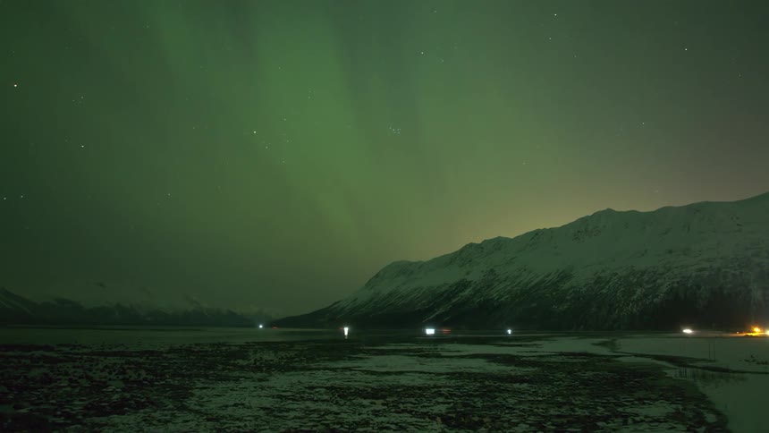 Cars drive below snow covered mountain northern lights in sky