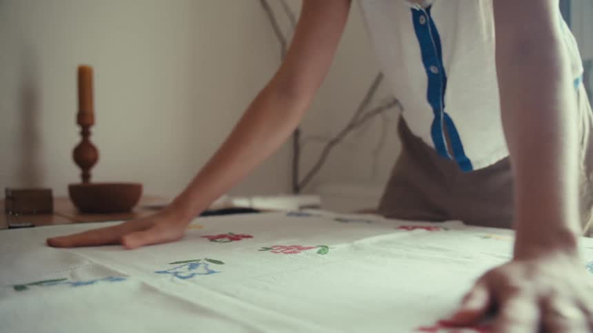 Woman standing up indoors covering a table with a cloth and then lining it with her hands during day time
