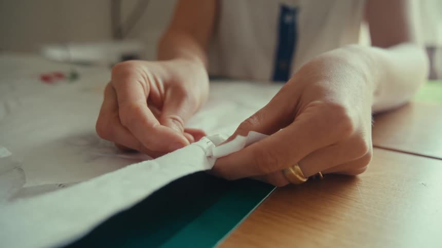 Woman with rings and white shirt sews two pieces of material together