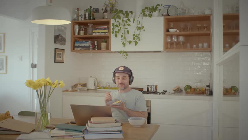 Man eats at dining table while watching laptop