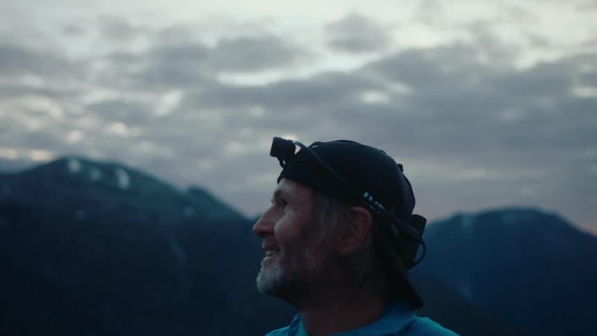 Portrait of an elderly person with a lantern on their head observing the sunrise in the mountains