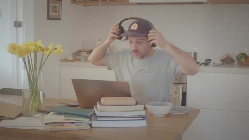A man sitting at a table talking on the phone then putting on and taking off headphones
