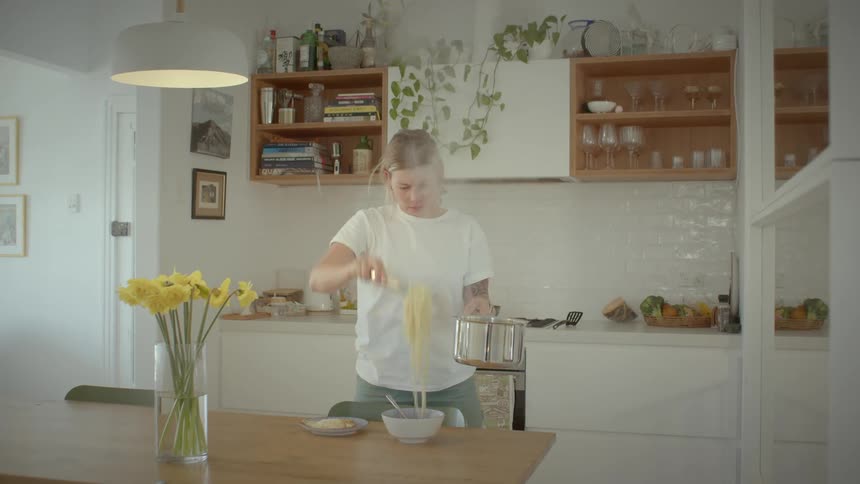 A woman taking pasta out of a pot and placing it in a bowl