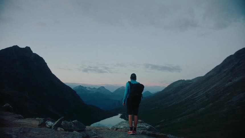 A man walking on top of a mountain and observing the landscape with lakes at sunrise