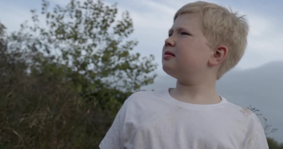 A boy stands outside on a breezy day