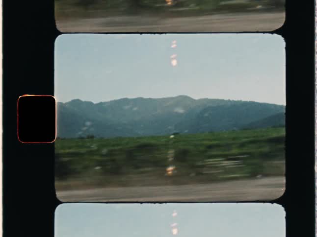 Super 8 film of a vacation, with vineyards and distant mountains are seen from a vehicle driving on country road