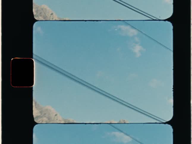 Super 8 film of distant rugged mountains seen from a vehicle driving on country road