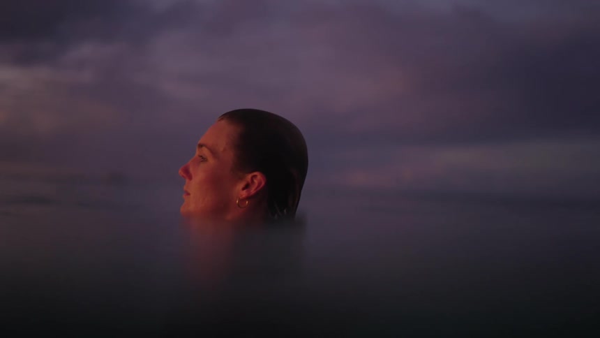 A young woman alone in the ocean at sunset