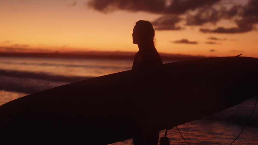 Young attractive girl walks out from the ocean at sunset after a surf