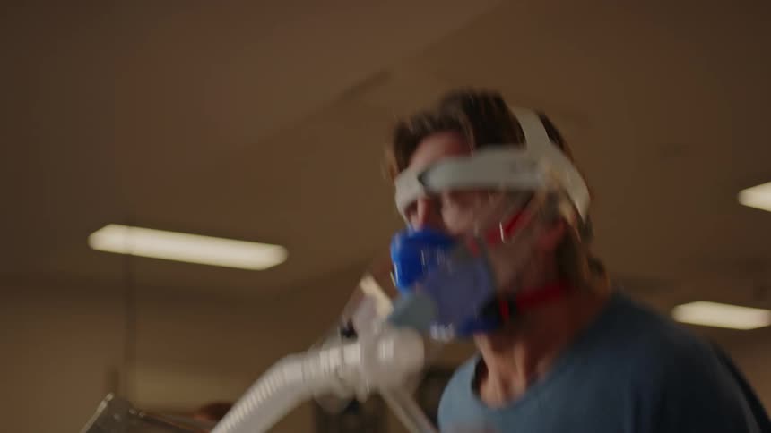 A man doing aerobic testing by running on a treadmill with a nose clip while being supervised by another man beside him