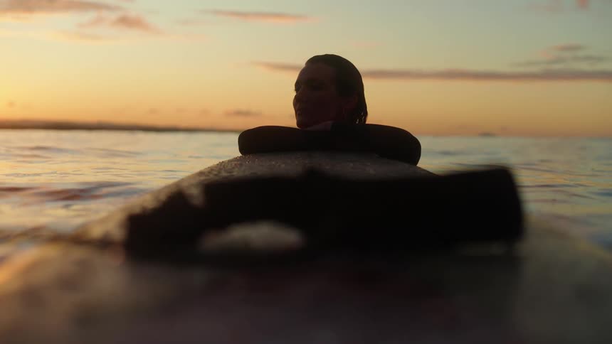 Beautiful young women resting on surf board in the ocean at sunset