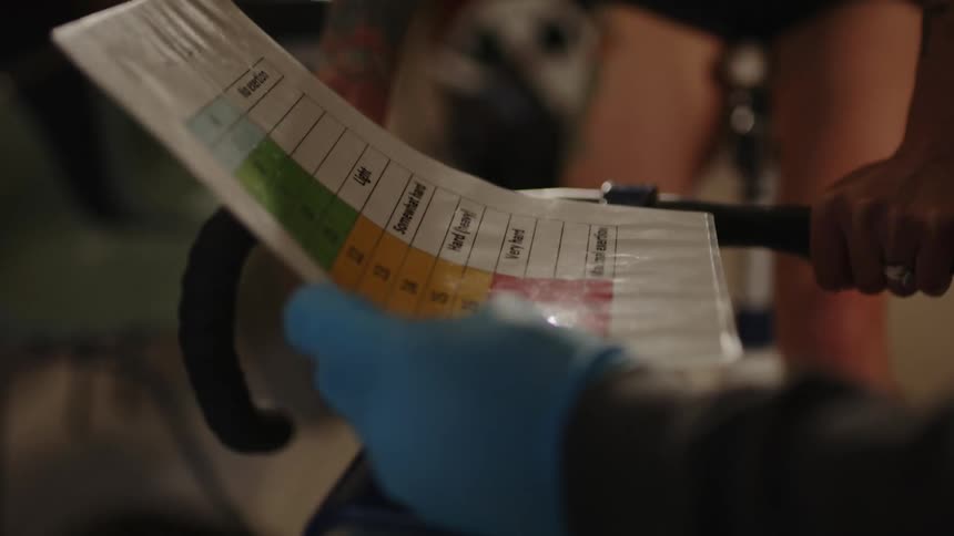 A woman pedaling on a bicycle undergoing a fitness test while receiving instructions from a person