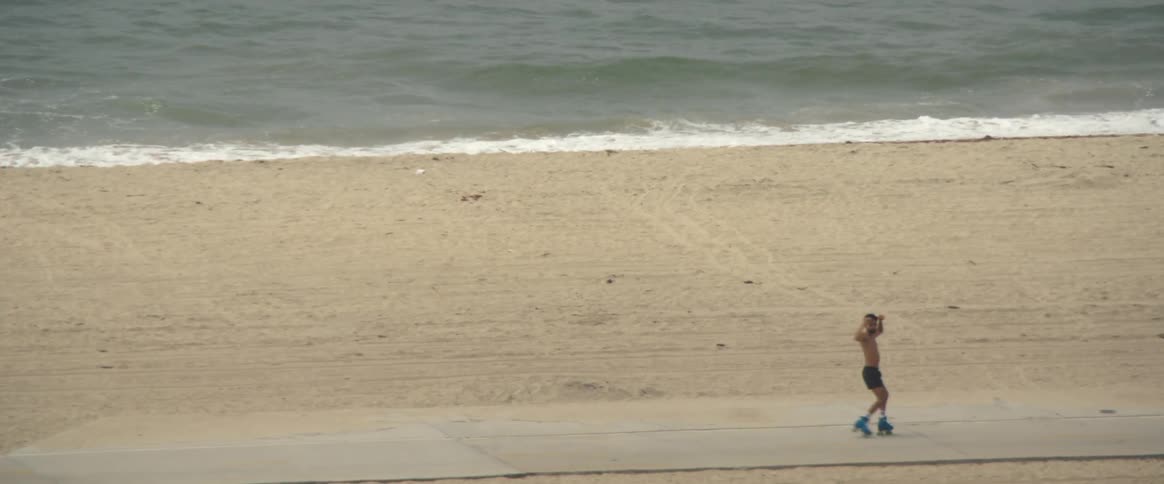 Shirtless man dancing on the beachside sidewalk with roller skates