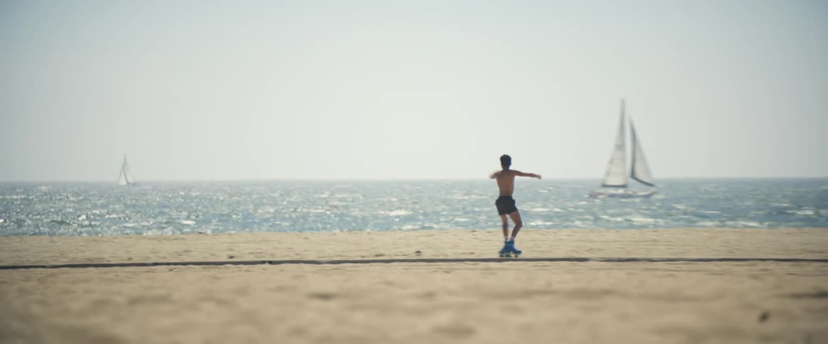 A man is spinning around as he rollerblades on the beach