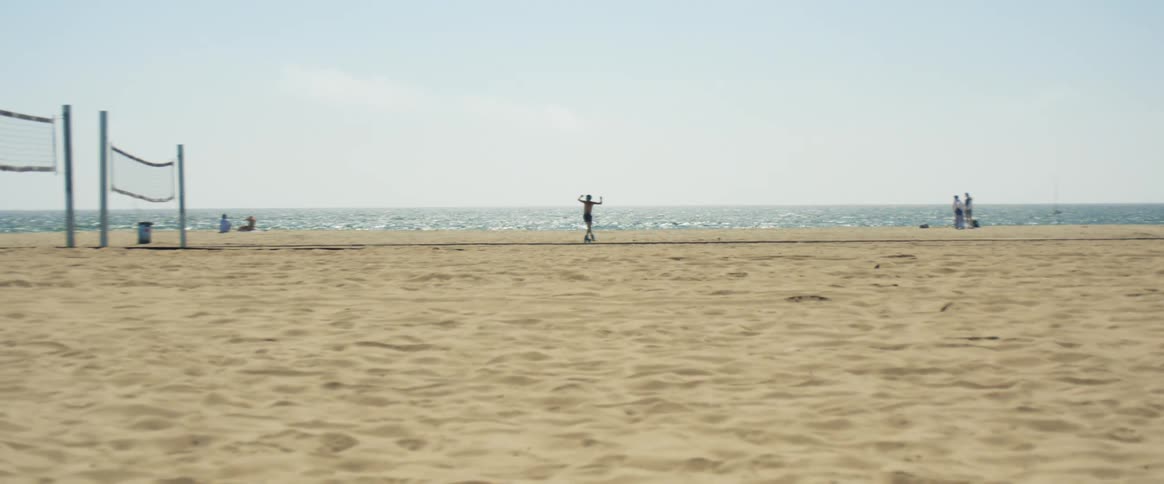 Man roller skates along beach path near sand volleyball court