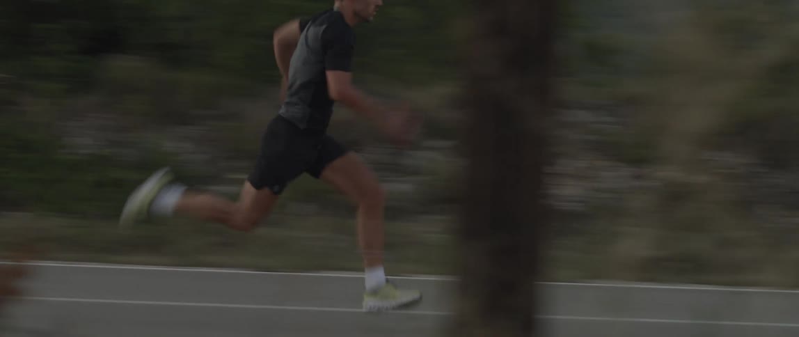 An adult man running quickly down a street wearing tennis shoes