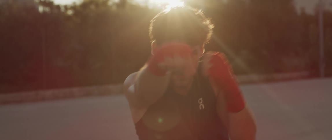 A man is outside wearing hand wraps practicing boxing moves in the air