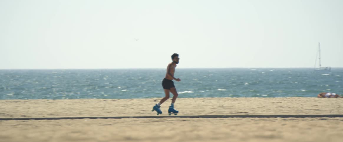A shirtless man skating near a beach on a sunny day