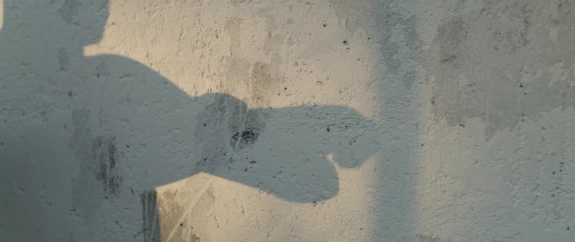 Shadow on a white wall of a man placing a band on his wrist and hand