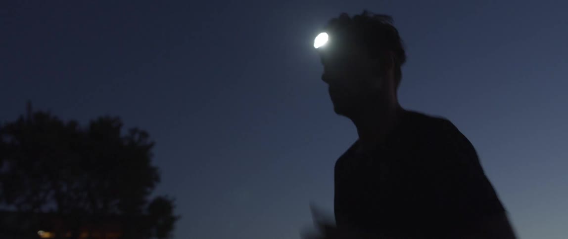 Male runner wears headlamp while running along street through neighborhood at night