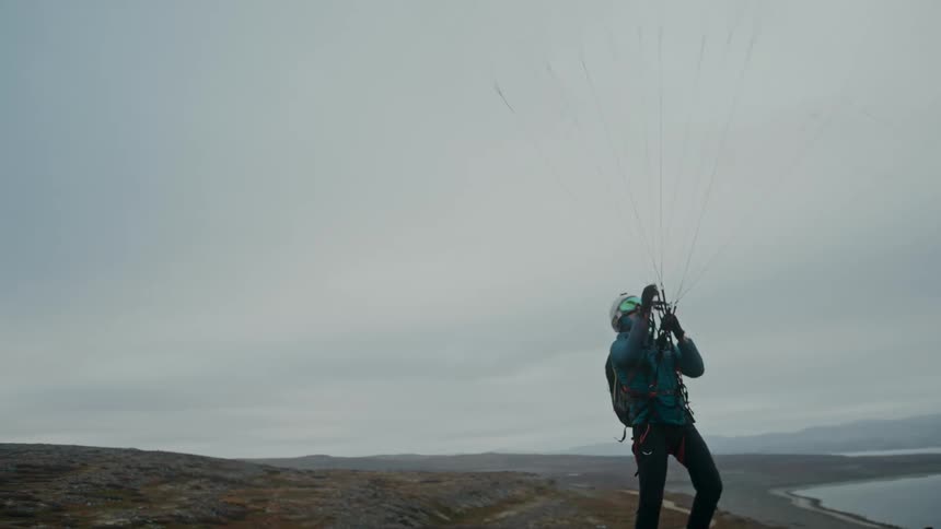 A man adjusting his parachute on top of a mountain peak on a cloudy day