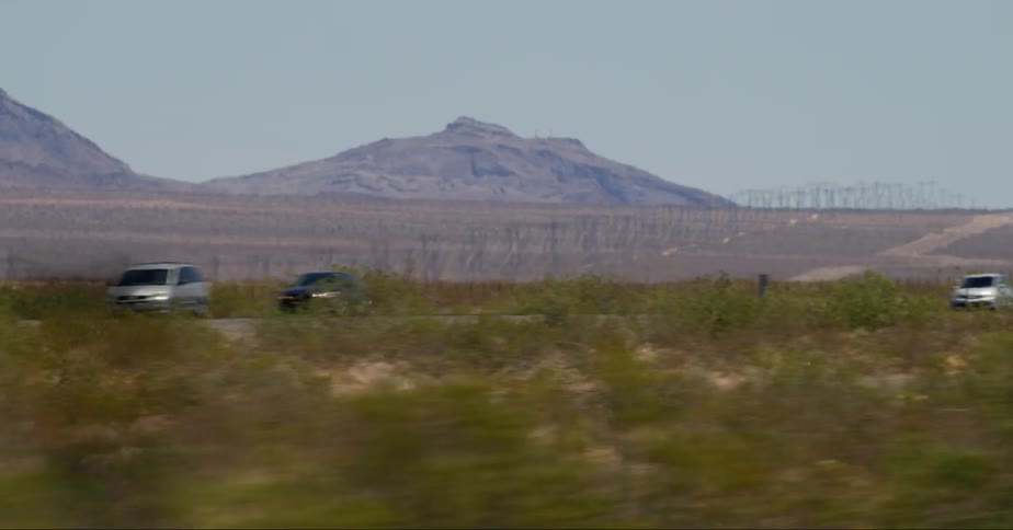 Vehicles drive on a road in the desert next to the mountains
