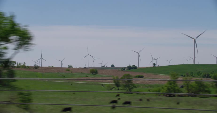 Turbines spin on a windfarm across a rural area among trees and vegetation