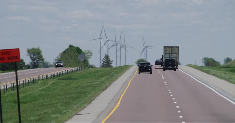 Cars drive down a street through a grassland with windmills on the side