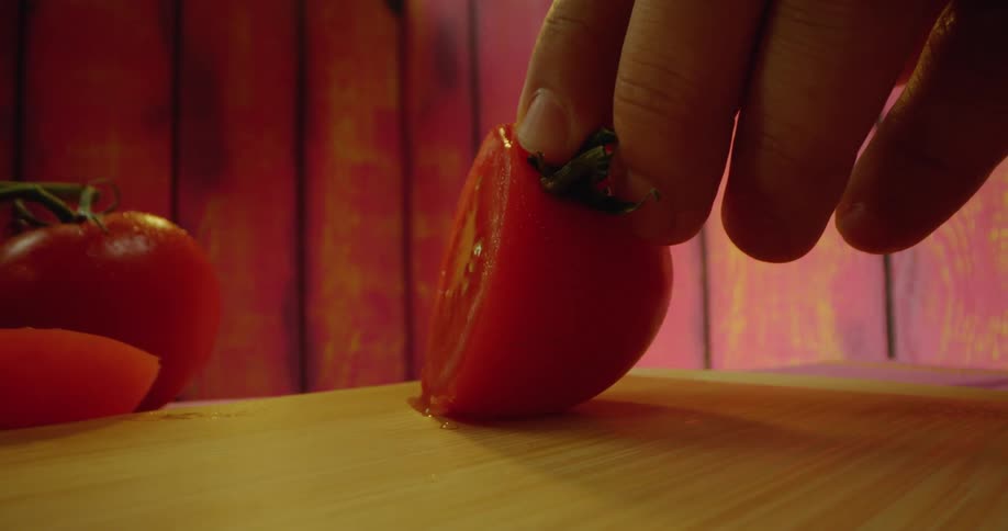 Closeup of a knife cutting a tomato on a wooden cutting board