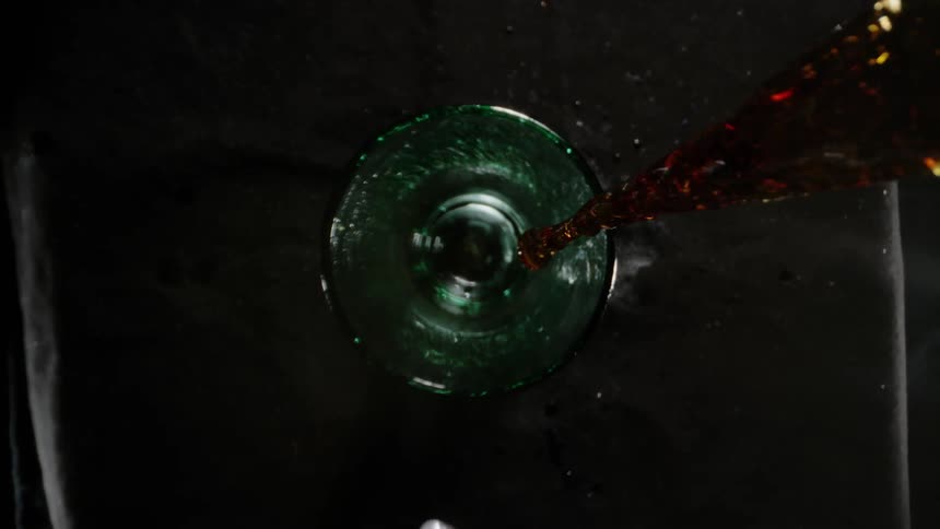 Soda pours from a bottle into a glass while ice cubes fall