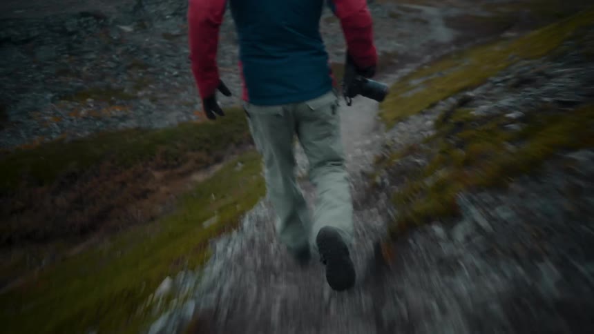 Male photographer runs along rock strewn path overlooking coast
