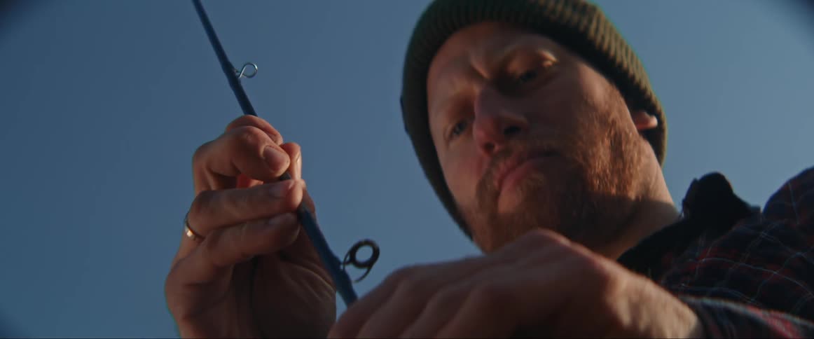 A man wearing a beanie concentrates on assembling his fishing rod