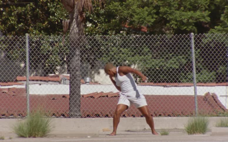 Woman with short hair white tank top and shorts dances in front of fences at the park