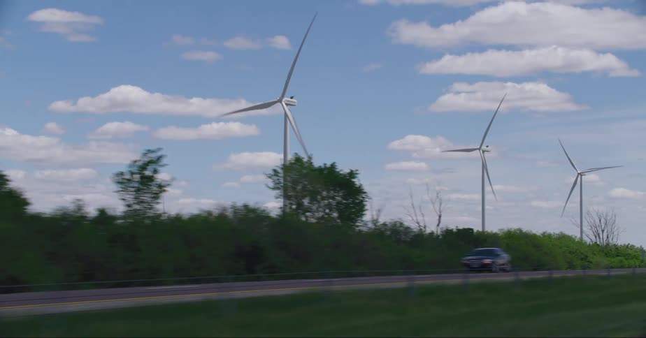 Spinning wind turbines overlook cars and trucks traveling on a road