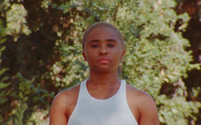 Woman with short hair and white tank top poses for the camera at the park