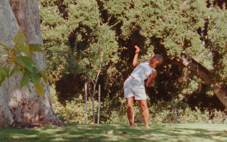 Woman with short hair white tank top and shorts dances at the park