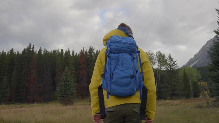 A man is hiking on some grass towards a forest