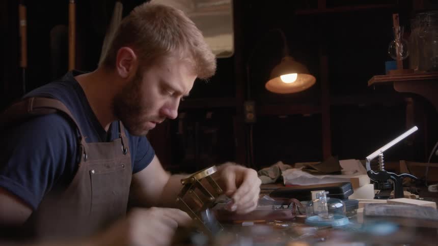 Man working with tools and a magnifier in an indoor workshop