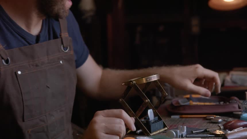 A male watchmaker carefully uses tools while in his workshop