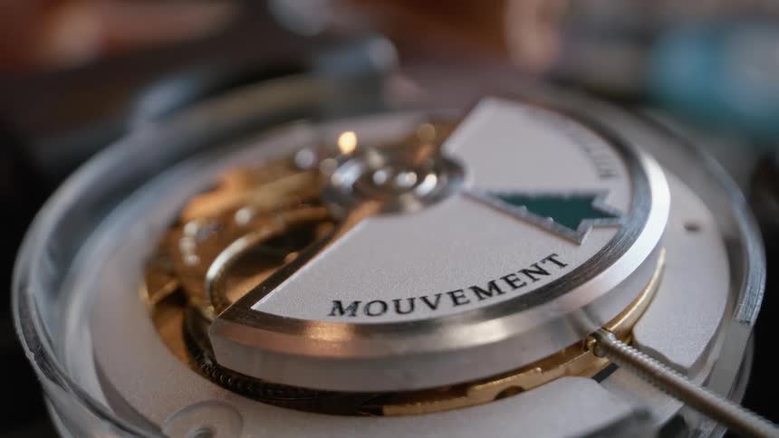 A persons hand holds tweezers and turns the inside of a clock with them