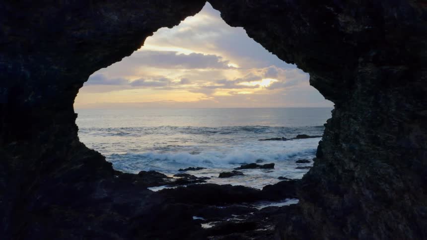 Rock formation with a hole faces ocean at sunset