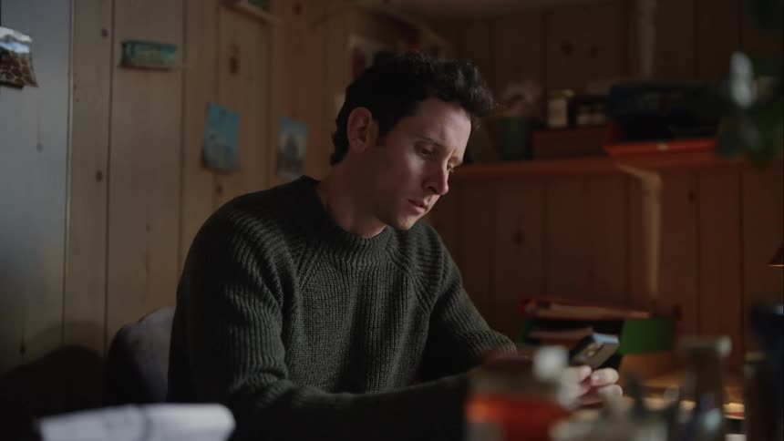 Man with gray sweater sits at table thinking and using smartphone