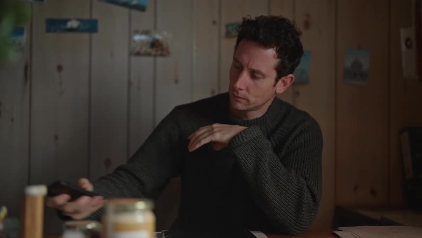 Man with gray sweater uses smartphone sitting at table thinking
