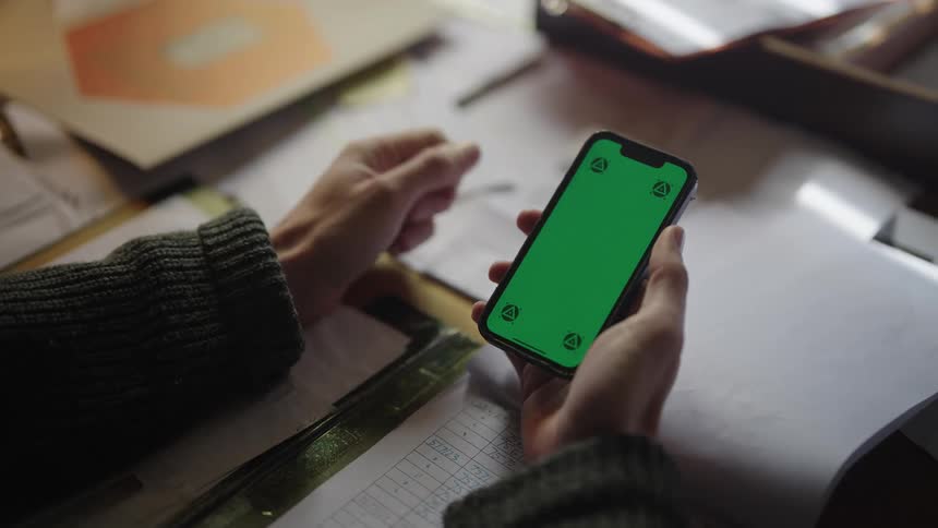 Man in gray sweater uses smartphone at desk
