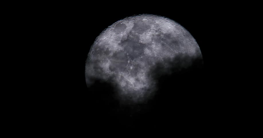 Clouds pass swiftly in front of a full moon at nighttime