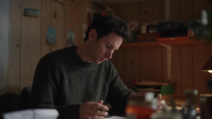 A man is sitting at a desk looking at paperwork and using a calculator