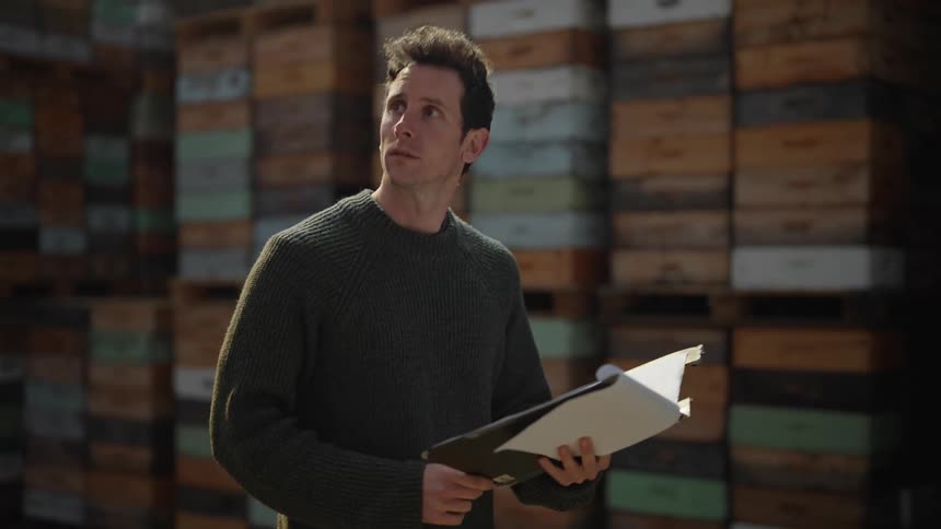 A man reads from a folder while walking through a warehouse stacked with boxes
