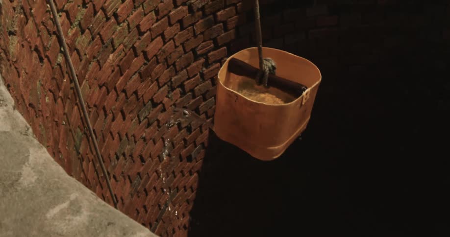 Person raises leaking water bucket from well